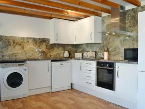 a kitchen with white cabinets and a washer and dryer at Ash Tree Cottage in Gillamoor