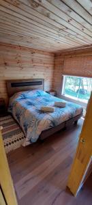 Bett in einer Holzhütte mit Fenster in der Unterkunft Cabaña La Troya in Cochamó