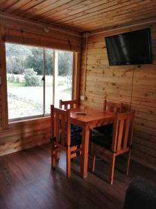 ein Esszimmer mit einem Holztisch und Stühlen sowie einem TV in der Unterkunft Cabaña La Troya in Cochamó