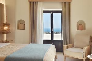 a bedroom with a bed and a chair and a window at Villa Irene Santorini in Vourvoulos