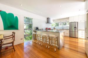 a kitchen with white cabinets and a bar with stools at Inside Out House in Oneroa