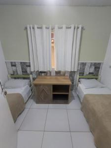 a room with two beds and a table and a window at Pousada São Judas Tadeu in Cachoeira Paulista