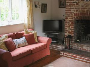a living room with a red couch and a television at Blacksmiths Cottages in Stiffkey