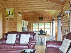a living room with a leather couch and a kitchen at Ashknowe Log Cabin - S4590 in Glenfarg