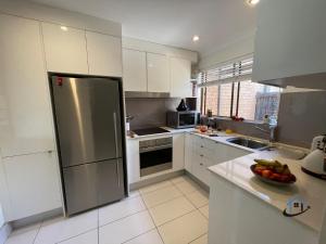 cocina con armarios blancos y nevera de acero inoxidable en Harbord House - Ocean views, plunge pool, 2 bed, free-wi-fi, superb location en Freshwater