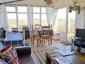 a living room with a table and chairs and windows at Les Quatre Vents in Dungeness
