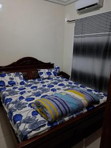 a bed with a blue and white comforter and a window at Hann Mariste in Dakar