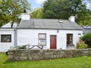 a white cottage with a red door and a stone wall at Llwyn Y Brig Isaf in Trevor