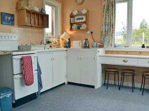 a kitchen with white cabinets and a counter with stools at The Cottage in Duirinish