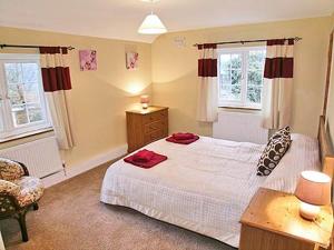 a bedroom with a bed and a chair and two windows at Well Cottage in Luxborough