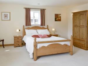 a bedroom with a wooden bed with white sheets at Bank Top Cottage in Cropton