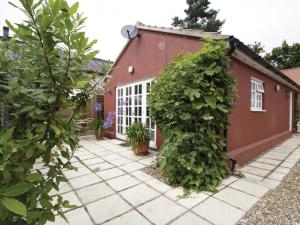 a garden with a red building and plants at Wisteria Cottage in Aylsham