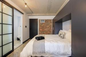 a bedroom with a large white bed with a brick wall at Manhattan On Coral Apartments in Bloubergstrand