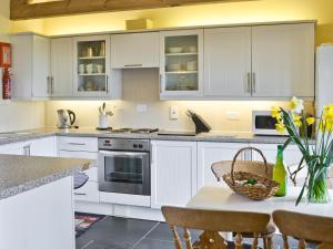 a kitchen with white cabinets and a table with yellow flowers at The Linhay in Milford