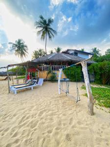 a beach with a swing and a house with palm trees at Little Pumpkin Cabanas in Tangalle