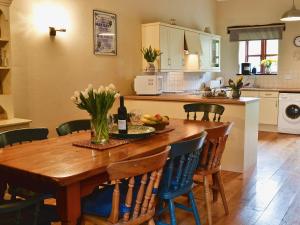 una cocina con una mesa de madera con flores y una botella de vino en The Linhay, en Trewen