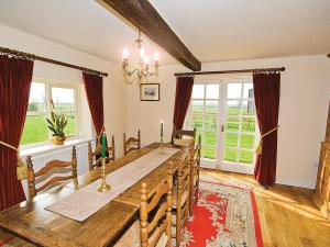 a dining room with a long wooden table and windows at Brook House Farm Cottage in Church Minshull