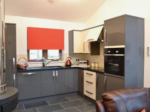 uma cozinha com armários cinzentos e uma cortina vermelha em Cairn View em Strachan