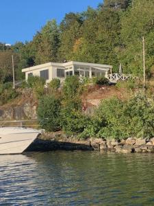 a house on a hill with a boat in the water at Renovated sea facing cottage on the Eidanger fjord in Porsgrunn