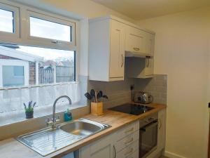 a kitchen with white cabinets and a sink and a window at Amberley Cottage in Alfreton