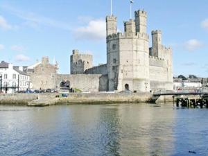 a large castle sitting on top of a body of water at Is Helen Cottage in Caernarfon