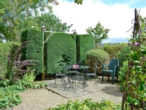 a table and chairs in a garden with a hedge at The Hunting Lodge in Wyck Rissington