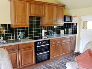 una cocina con armarios de madera y horno negro en Dyke Heads Stable, en Gunnerside
