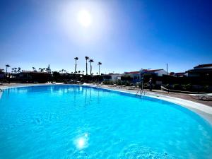 a large blue swimming pool with the sun in the background at Escarabajo Bungalow il Maggiolino in Maspalomas