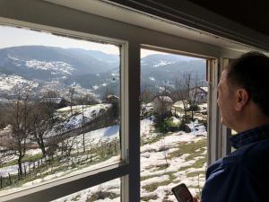 un homme qui regarde par une fenêtre les montagnes enneigées dans l'établissement Tarihi Karadeniz Evi, à Ayancık