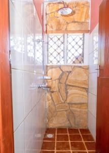 y baño con ducha y pared de piedra. en Rudi House en Msaranga