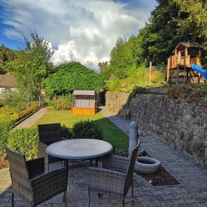 a patio with a table and chairs and a stone wall at Ferienhaus am Bach mit großem Garten in Deuerling