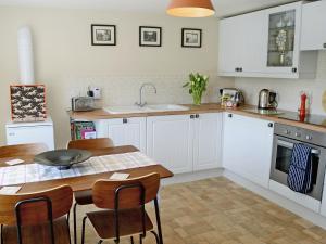 a kitchen with white cabinets and a table and chairs at The Wee Hoose in Achnahanat