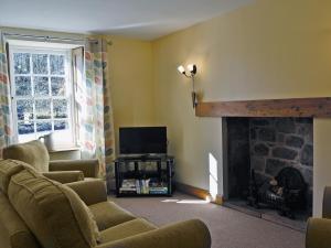 a living room with a fireplace and a tv at Waulkmill Cottage in Carronbridge