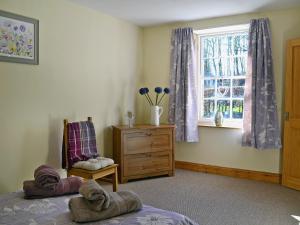 een slaapkamer met een bed, een raam en een stoel bij Waulkmill Cottage in Carronbridge