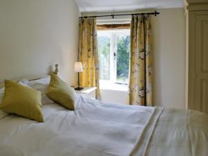 a white bed with yellow curtains and a window at Bank Cottage in Grindleford Bridge