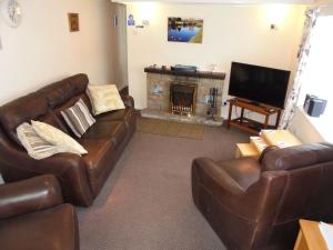 a living room with a leather couch and a fireplace at The White Cottage in Furness Vale