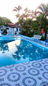 a blue swimming pool with a tile floor and palm trees at Pousada Ancora in Vera Cruz de Itaparica