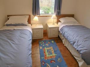 two beds in a room with two lamps and a rug at Middledrift Cottage in Brora