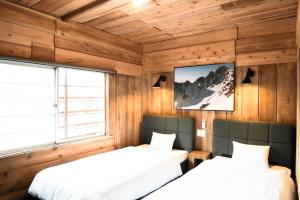 two beds in a room with wooden walls at Guesthouse Shimashima in Matsumoto