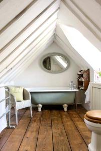 uma casa de banho com uma banheira e um espelho num sótão em The Old Bakehouse Cotswold Cottage em Stonesfield