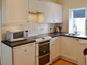 a kitchen with white cabinets and a microwave at Limpet Cottage in Boulmer
