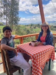 a man and a woman sitting at a table on a porch at Refugio de Guacheneque, Glamping y Hospedaje Rural in Villapinzón