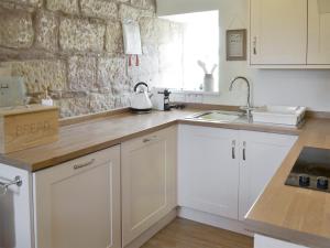 cocina con armarios blancos y pared de piedra en West View Cottage, en Seahouses