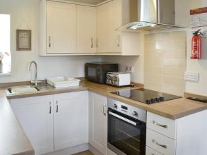 a kitchen with white cabinets and a sink and a microwave at West View Cottage in Seahouses