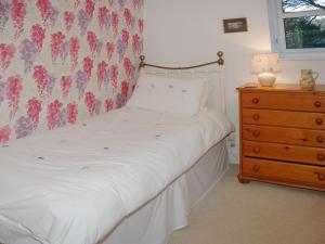 a bedroom with a white bed with a dresser and a window at Chapelfield Cottage in Rosthwaite