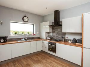 a kitchen with white cabinets and a clock on the wall at Three The Old Stables in Knitsley