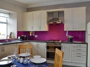 a kitchen with white cabinets and purple walls at The Boathouse in Findochty
