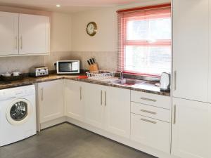 a kitchen with white cabinets and a sink and a microwave at Willow Cottage in Corpusty