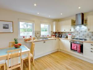 cocina con armarios blancos, mesa y sillas en Barn Owl Cottage - 27941, en Cambusbarron