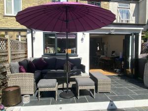 - un parasol violet sur une terrasse avec un canapé et des chaises dans l'établissement Three Bedroom Family home with garden in Walthamstow, à Londres